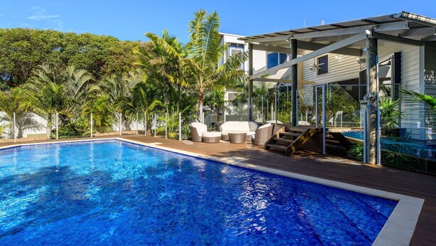 Ein Pool mit Holzterrasse, Gartenmöbeln und einem überdachten Sitzbereich.