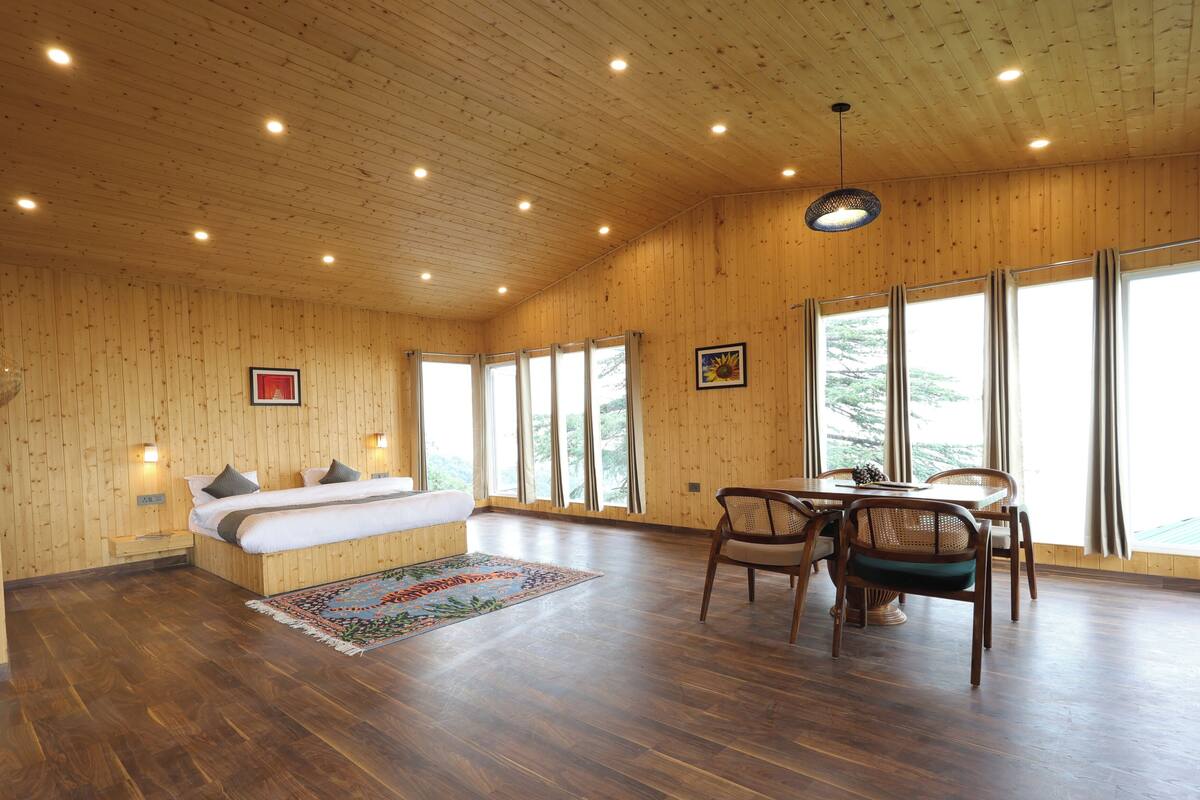 Een kamer met houten lambrisering, een bed, een eettafel met stoelen en grote ramen.
