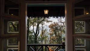An open doorway leading to a balcony with a table and chair, overlooking a forested area. - Sansa By The Woods - Manor Mussoorie (Mussoorie)