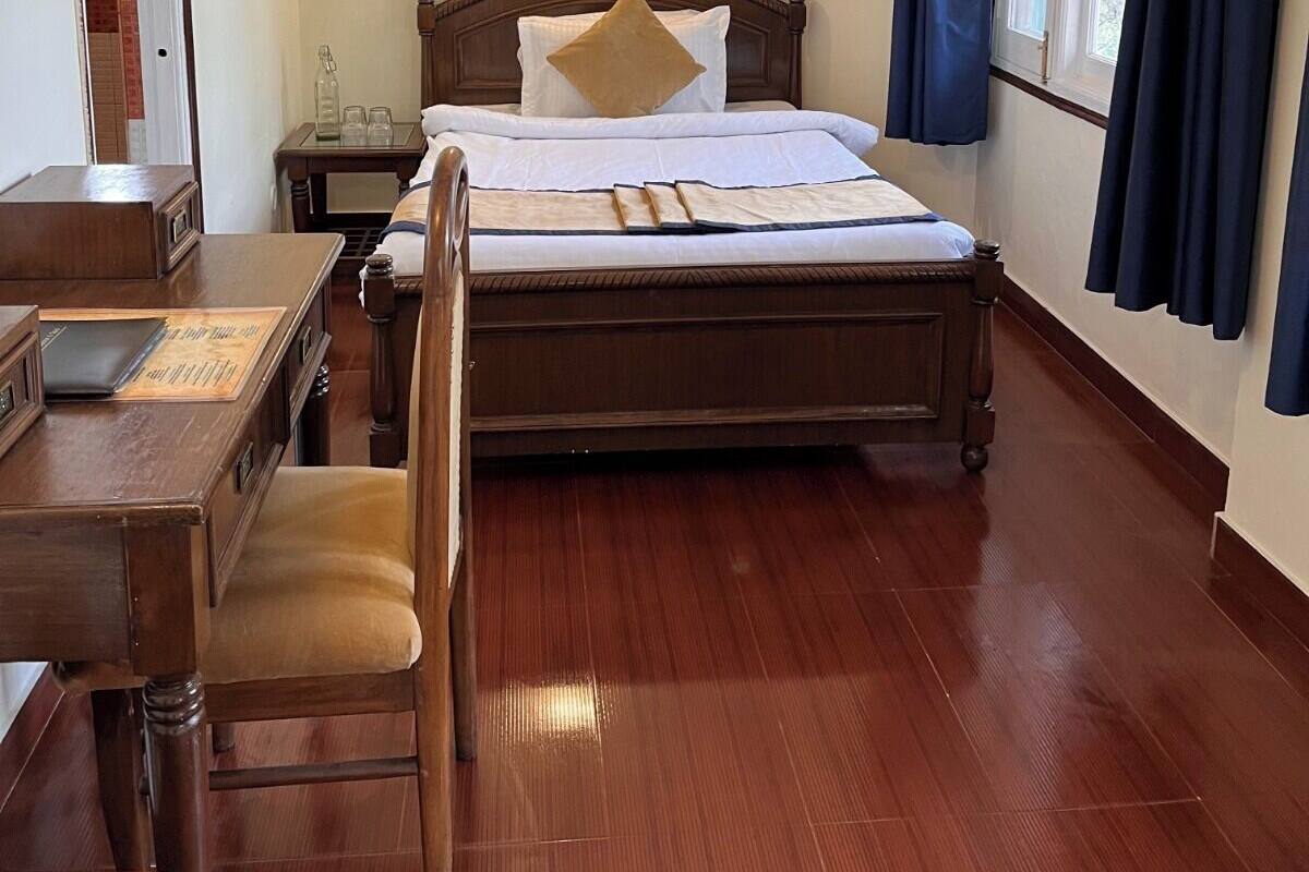 Een hotelkamer met een houten bed, een bureau, een stoel, een nachtkastje, een lamp en een raam met gordijnen.