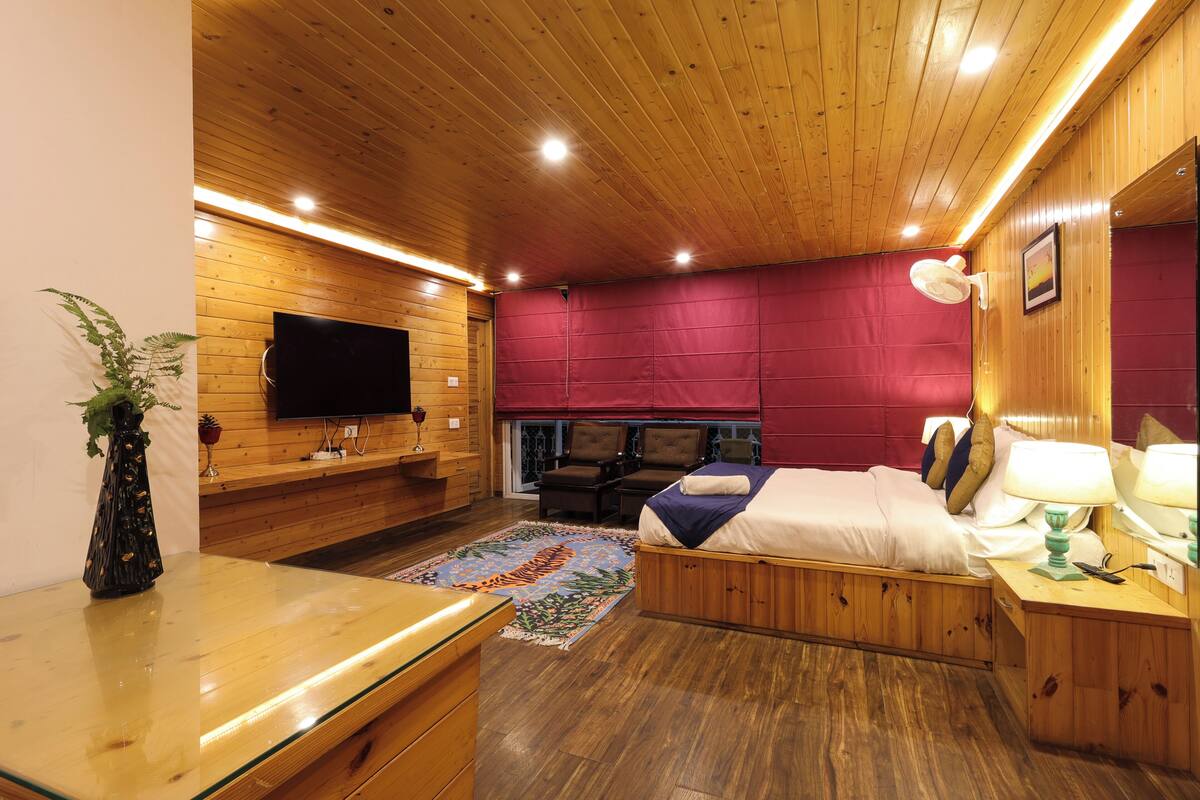 Een kamer met houten lambrisering, een bed, nachtkastje, lamp en een wandgemonteerde flatscreen televisie.