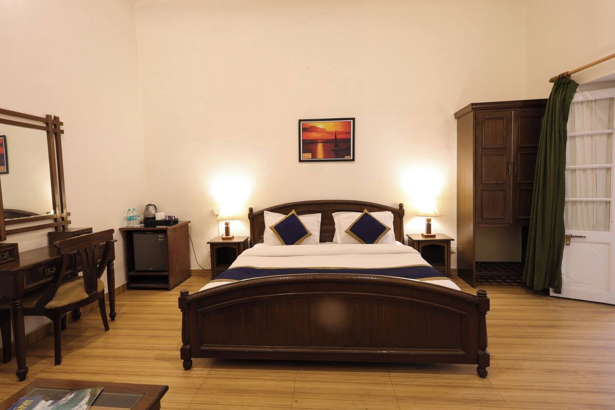 Een slaapkamer met een houten bed, nachtkastjes, een bureau, een stoel, een spiegel en een schilderij aan de muur.