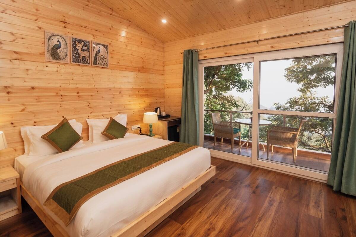 Een kamer met houten lambrisering, een groot bed, een nachtkastje, een tafel en een raam met uitzicht op bomen.