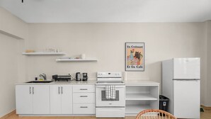 A modern kitchen with white cabinets, a stove, a refrigerator, and a wicker chair.