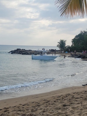 A beach with a boat, rocky outcrops, and people. - WaveView-1 |1 BR Condo |Ocean View | Generator (Rincon)