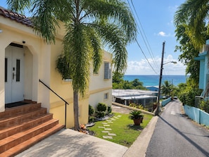 A residential property with a staircase leading to a door, a small garden with a pathway, and a view of the ocean. - WaveView-1 |1 BR Condo |Ocean View | Generator (Rincon)