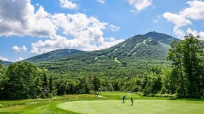 Ein Golfplatz mit Bergblick, blauem Himmel und üppigem Grün.