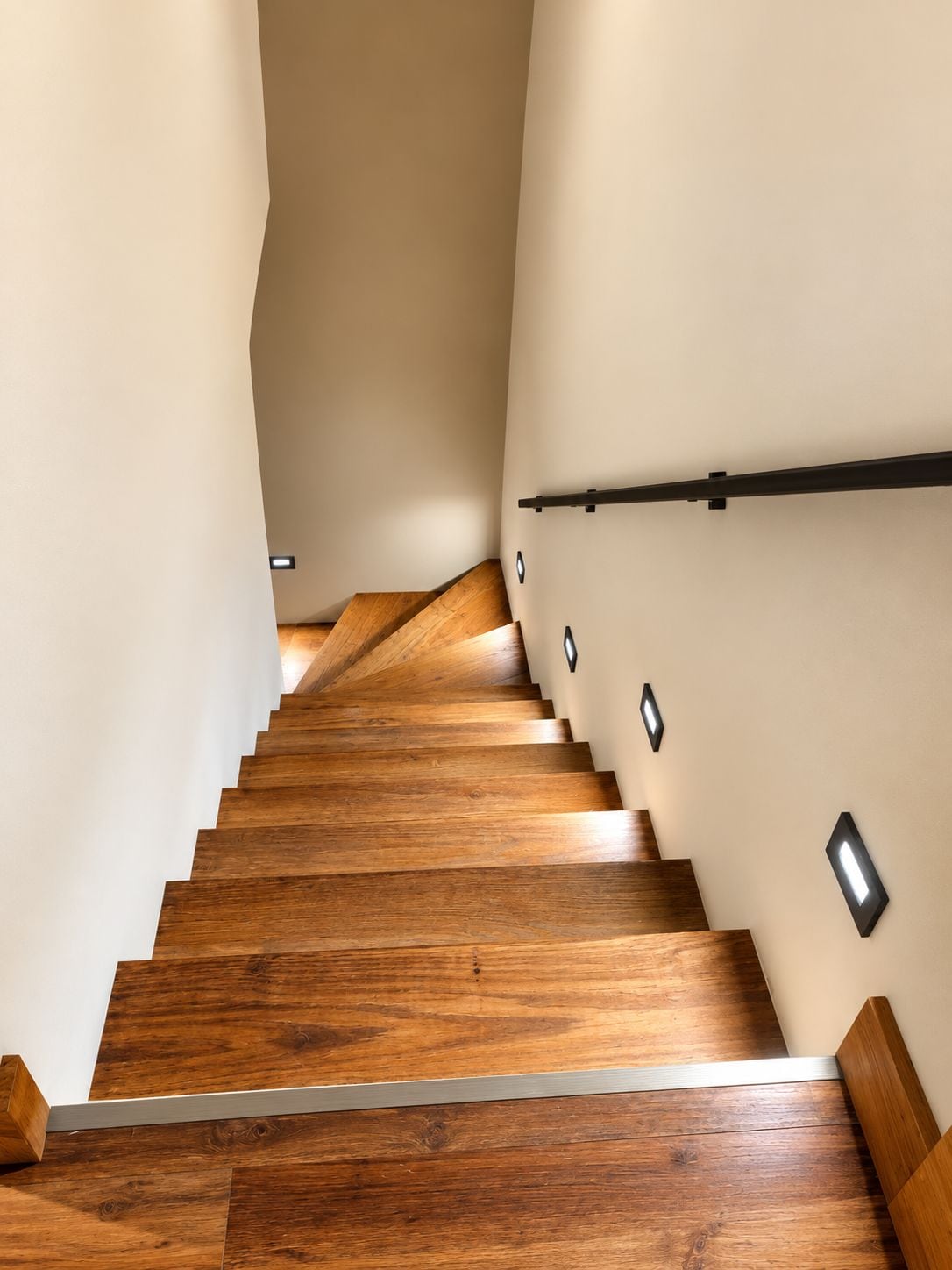 Eine Holztreppe mit Handlauf und Wandleuchten.