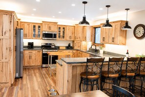 A kitchen with wooden cabinets, stainless steel appliances, a bar area with stools, and pendant lighting. - Brand new Ski Chalet 4 miles to Jay Peak (Jay)