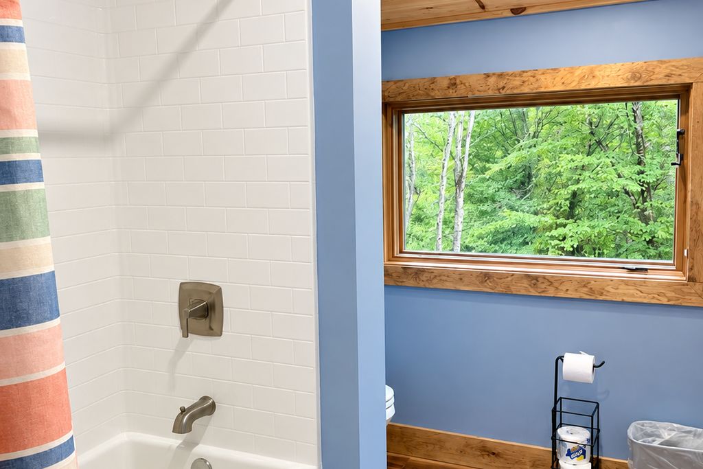 Une salle de bain avec une baignoire, une fenêtre donnant sur la verdure et un porte-serviettes avec un rouleau de papier toilette.