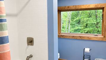A bathroom with a bathtub, a window with a view of trees, and a towel rack with a roll of toilet paper.