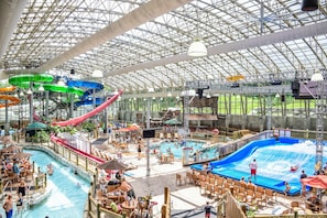 Parque acuático interior con múltiples piscinas, toboganes y una zona cubierta con asientos.