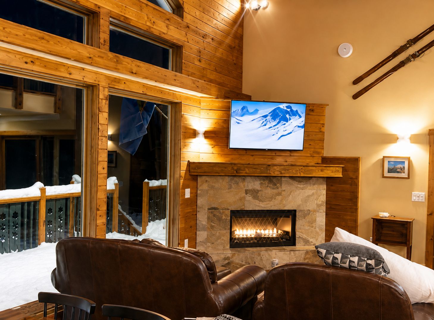 Un intérieur chaleureux avec une cheminée, des fauteuils en cuir, un téléviseur et une vue sur le paysage enneigé.