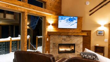 A cozy interior with a fireplace, leather seating, a television, and a view of the snowy outdoors.