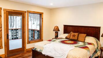 A bedroom with a wooden bed, a window with a view of trees, and a door with a railing.