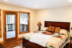 Un dormitorio con cama de madera, ventana con vista a árboles y una puerta con barandilla.