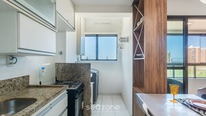 A compact kitchen with a granite countertop, a built-in stove, and a window providing a view of the city.