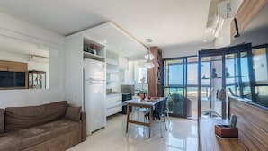 A modern kitchen with white cabinets, a dining area with a table and chairs, and a large window offering a view of the ocean.