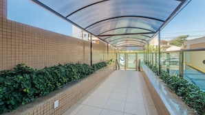 A covered walkway with tiled flooring, bordered by brick walls and green shrubs.
