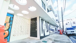 Un edificio con diseño moderno, que presenta luces circulares en el techo, una pared con textura y una puerta de malla metálica.