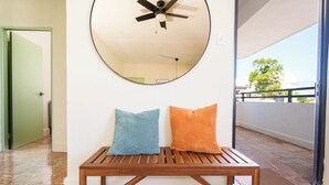 Una habitación con un banco de madera, dos almohadas, un ventilador de techo y un espejo grande en la pared.