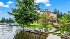 A house by a lake with a dock, surrounded by trees and a well-maintained lawn.