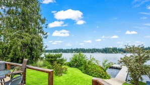 A deck with a view of a lake, surrounded by greenery and a wooden railing.
