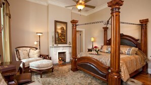 Een ruime slaapkamer met een hemelbed, een openhaard en een klassieke kroonluchter.