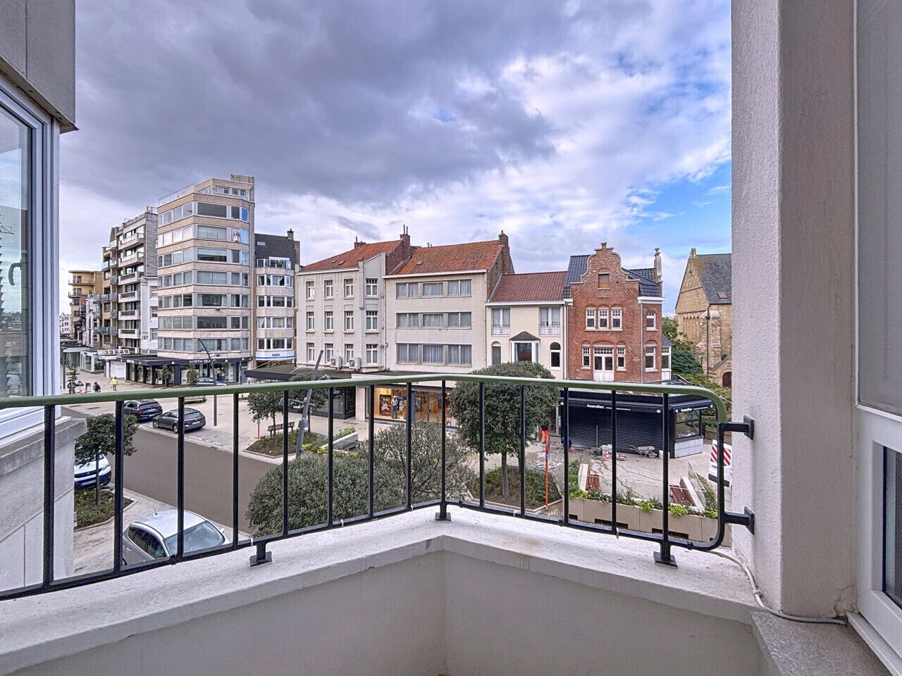 A balcony with a view of a city street, featuring multi-story buildings and a clear sky.