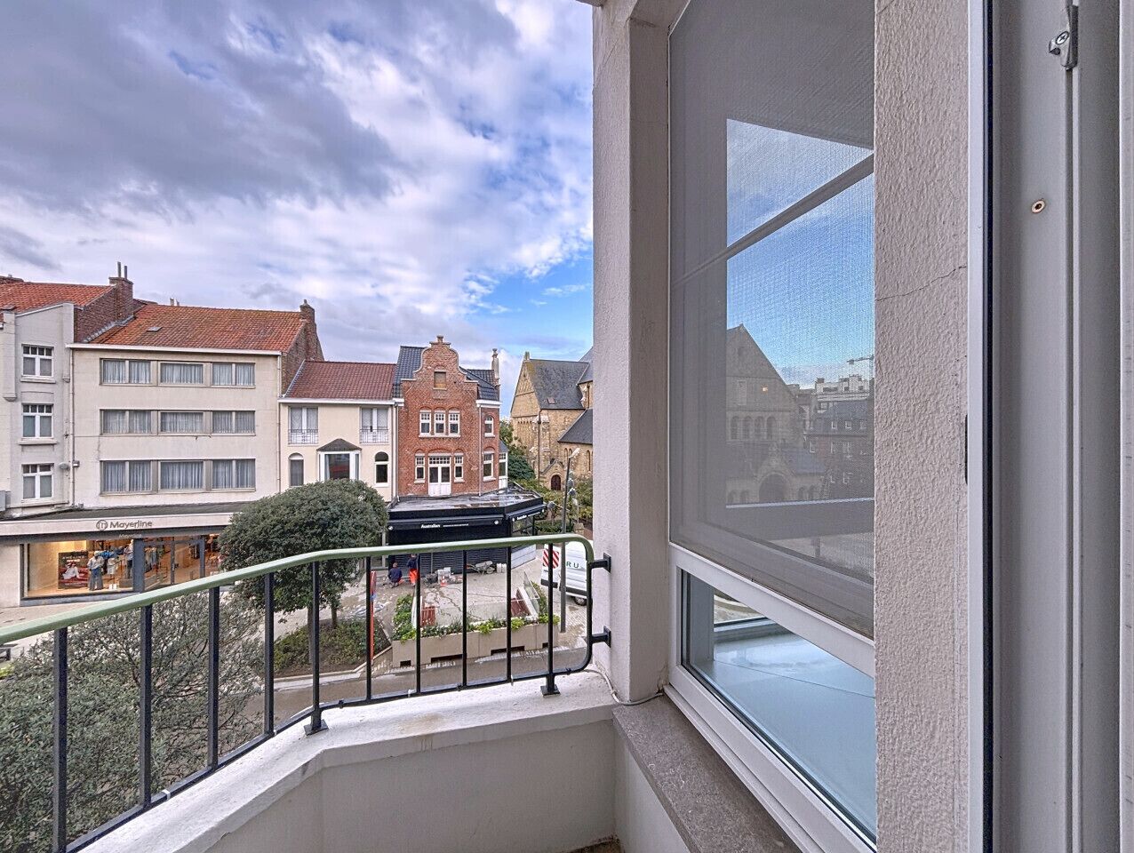 A balcony with a view of a street, buildings, and a clear sky.