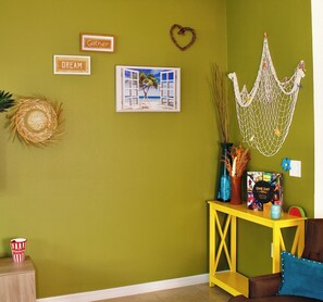 A room with a green wall, a yellow console table, a framed picture, and wall decorations including a heart-shaped wreath and signs with words 'Gather' and 'Dream'.