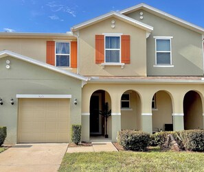 A two-story residential building with a garage, arched entryway, and a covered patio area.