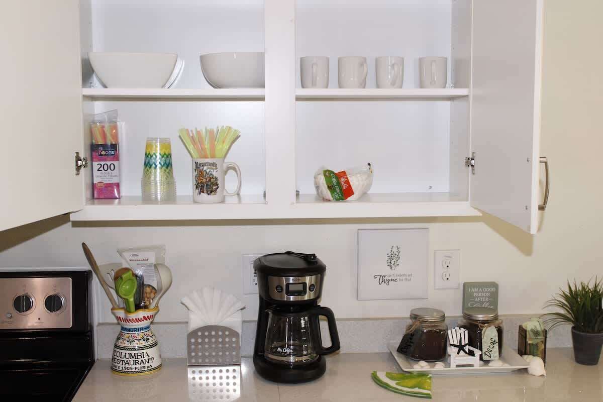 A kitchen with white cabinets, a coffee maker, a grater, and various kitchen utensils.