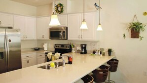 A modern kitchen with white cabinets, stainless steel appliances, pendant lighting, and a central island with bar stools.