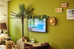 A room with a wall-mounted TV displaying a beach scene, a wooden side table with decorative items, and a green wall.
