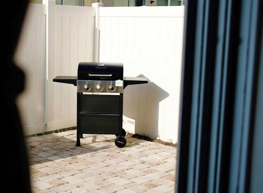 Ein schwarzer Grill mit vier Brennern auf einer gepflasterten Terrasse, im Hintergrund ein weißer Zaun.