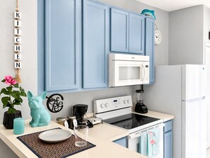 A kitchen with blue cabinets, a white microwave, a stove, and a refrigerator.