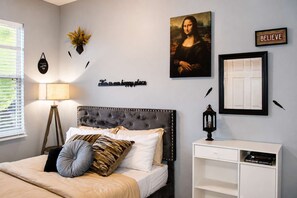 Une chambre à coucher comprenant un lit, une table de chevet, une lampe, une œuvre d’art accrochée au mur et un tableau encadré.