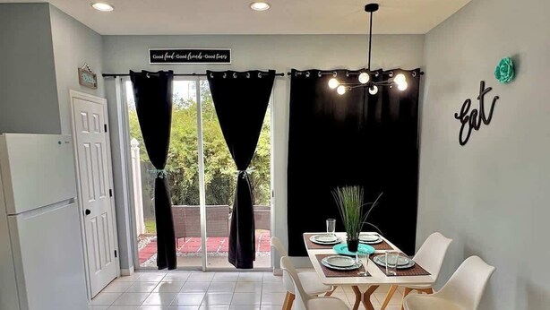 A modern kitchen with a dining area, featuring a dining table set for four, a refrigerator, and a sign with positive phrases. - Level Up Your Vacation! Stylish Home Near Disney (Kissimmee)