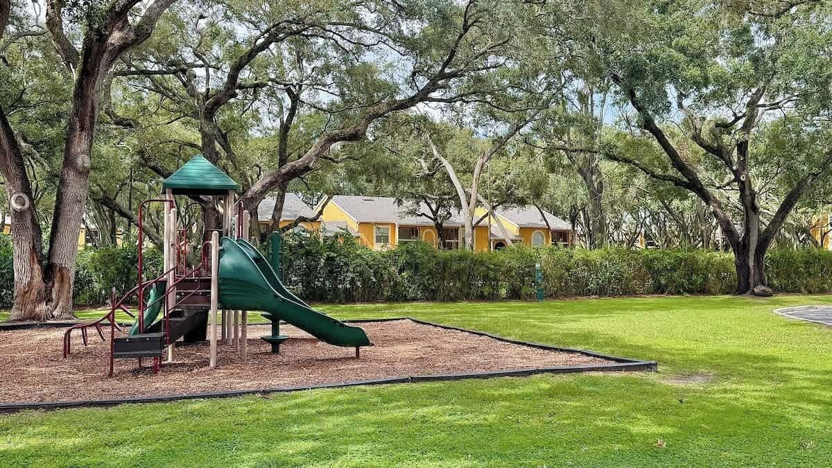 Ein Spielplatz mit Rutsche und Klettergerüsten, umgeben von Bäumen und einem gepflegten Rasen.