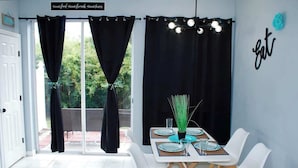 A dining area with a table set for four, black curtains, and a sign on the wall. - Level Up Your Vacation! Stylish Home Near Disney (Kissimmee)