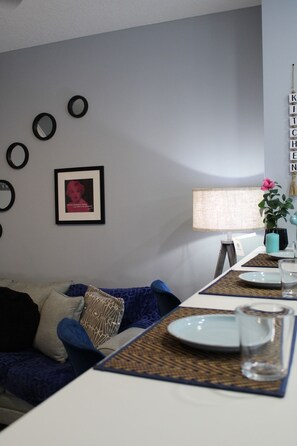 A modern living room with a sofa, a dining table set with plates and glasses, a lamp, and a wall with circular mirrors and a framed picture.