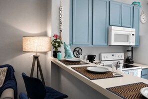 Une cuisine avec un four à micro-ondes blanc, une cuisinière et une machine à café. Il y a un meuble bleu au-dessus de la cuisinière et une horloge fixée au mur.