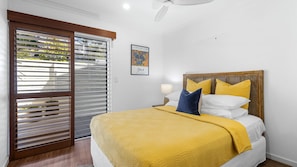Une chambre à coucher avec un lit, une table de chevet, une lampe et une fenêtre avec des stores.