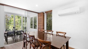 Un comedor con una mesa y sillas de madera, un separador de vidrio y vistas a zonas verdes a través de las ventanas.