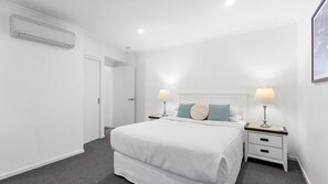 Ein Schlafzimmer mit einem Bett, zwei Nachttischen, einem Schreibtisch und einer Klimaanlage sowie einer Tür.