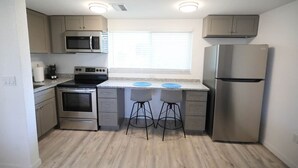 Una cocina funcional con microondas, estufa, refrigerador y dos taburetes de bar.