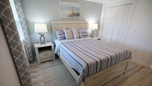 Un dormitorio con una cama, mesitas de noche, una lámpara, un cuadro en la pared y un armario.