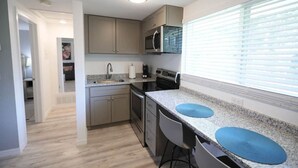 Una cocina moderna con encimera de granito, electrodomésticos de acero inoxidable y una ventana con persianas.