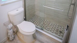 Ein Badezimmer mit Toilette, einer Dusche mit Glastür und einem Fenster.